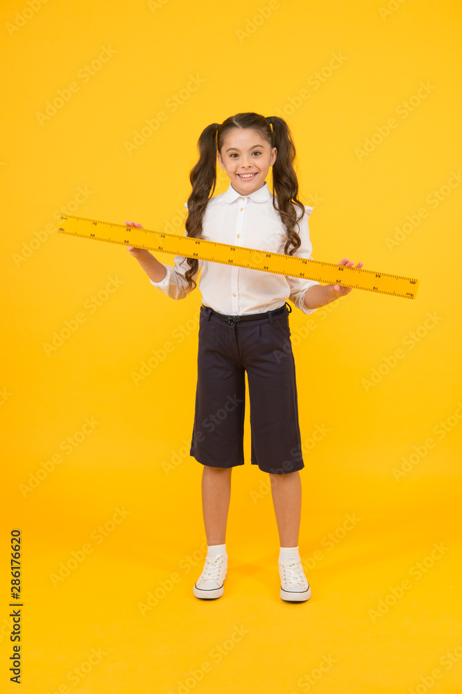 Education and school concept. Sizing and measuring. Studying is fun. School adorable student study geometry. Kid school uniform hold ruler. Pupil cute girl with big ruler. Geometry school subject Education and school concept. Sizing and measuring. Studying is fun. School adorable student study geometry. Kid school uniform hold ruler. Pupil cute girl with big ruler. Geometry school subject