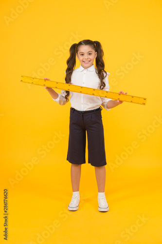 Education and school concept. Sizing and measuring. Studying is fun. School adorable student study geometry. Kid school uniform hold ruler. Pupil cute girl with big ruler. Geometry school subject