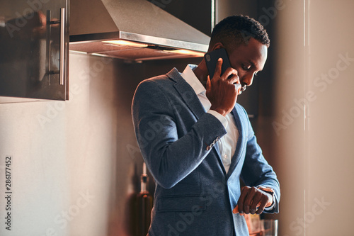 Slika na platnu Young african man in white shirt is chatting by mobile phone at the kitchen