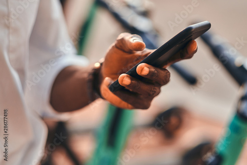 Closeup photo shoot of african man's hands with mobile phone. He is choosing the right scooter.