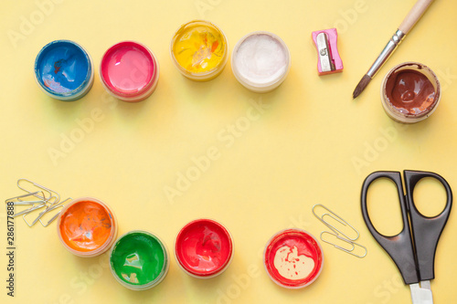 Colorful sample paints pots with scissors and tassel on yellow background. Copy space, flat lay.