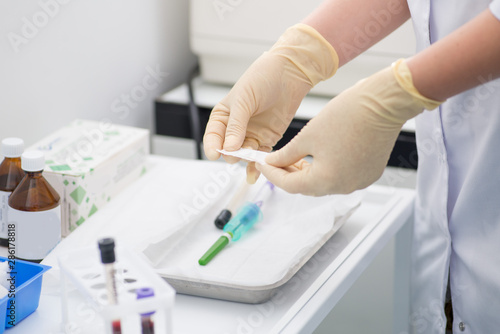 gloved laboratory assistant preparing for blood sampling against a background of blood tubes © smirart
