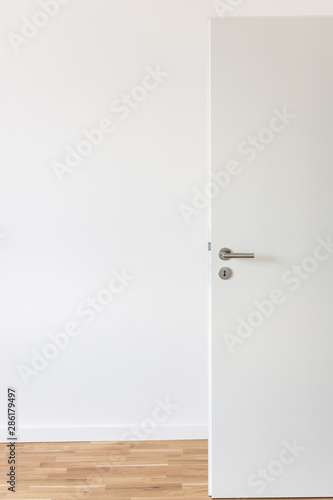 Open white door with a gray chrome handle and keyhole against a white wall in the room
