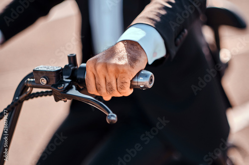 Elegant man in black suit and white shirt is driving electrical bike, selective focuse on hand.