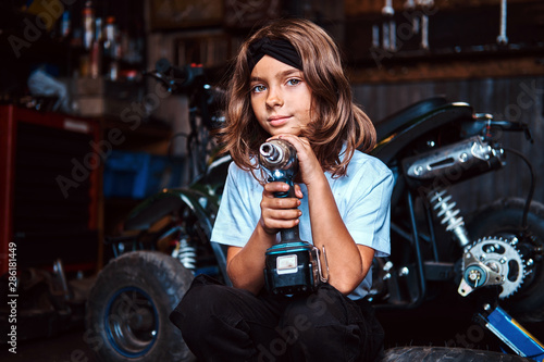 Pensive beautivul kid is posing with screwdraiver at auto service workshop. photo