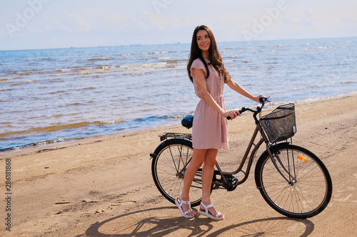 Young beautiful woman is enjoying summer with her bicycle at the seaside on the bright sunny day.