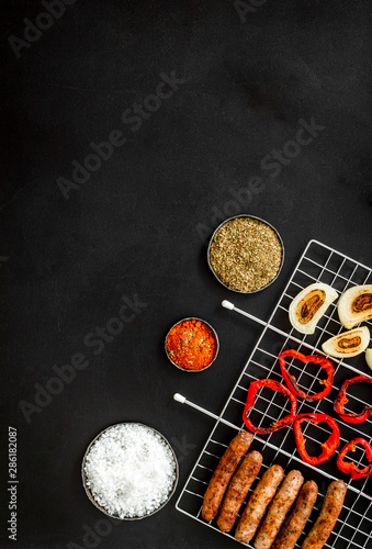 Barbecue with sausages, vegetables on grid and spices on black background top view copyspace