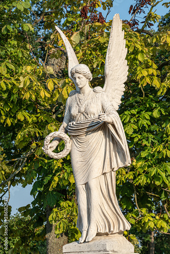 Statue of ancient beautiful winged angel in downtown park of Potsdam in beginning of Autumn at sunset, Germany