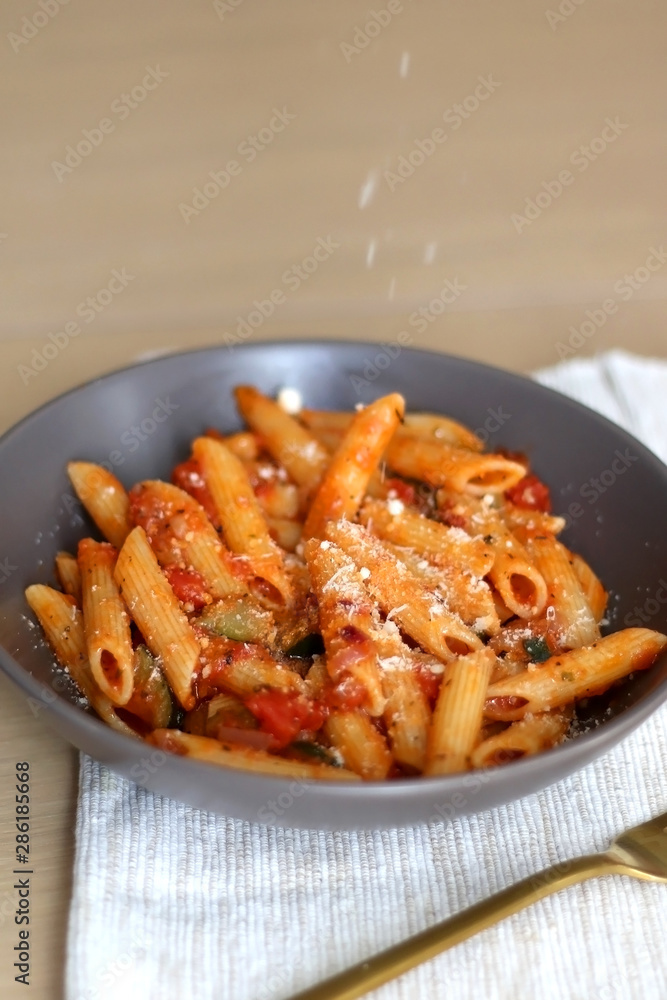 Sprinkling parmesan cheese on a plate of pasta with tomato sauce and eggplant. Selective focus. Sprinkling parmesan cheese on a plate of pasta with tomato sauce and eggplant. Selective focus.
