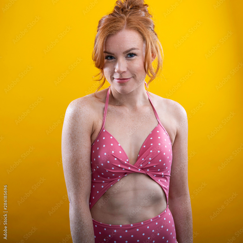 Cute girl with red hair and freckles wearing a pink polka dot bikini with a  yellow background Stock Photo | Adobe Stock