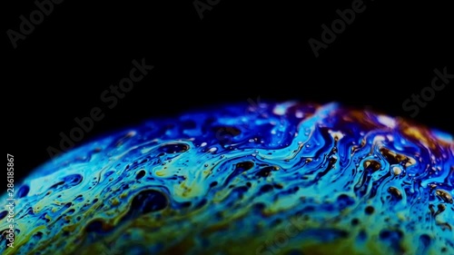 Multicolored rainbow colors of a single soap bubble that looks like a fantasy planet isolated against a black background