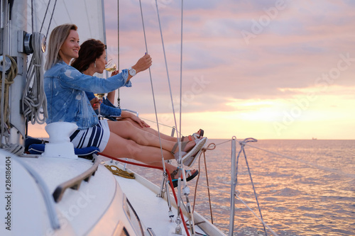 Two joyful women are celebraiting good summer day at the yacht while watching beautiful sunset. photo