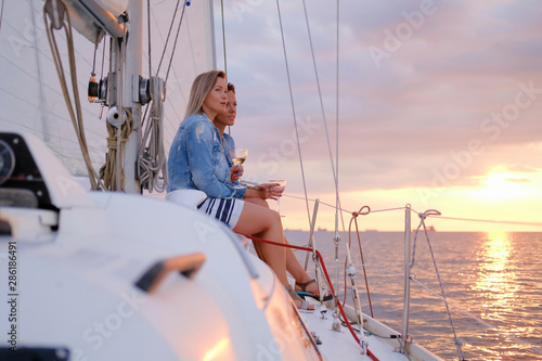 Two joyful women are celebraiting good summer day at the yacht while watching beautiful sunset. © Fxquadro