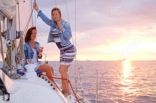 Pair of best friend are taking boat trip on the yacht at suset time with few glasses of wine.