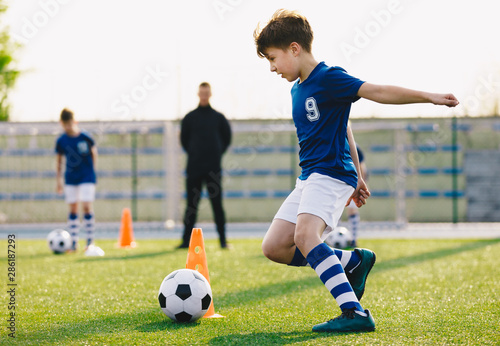 Fototapeta Naklejka Na Ścianę i Meble -  Children training football dribbling in a field. Kids Running the Ball. Players develop soccer dribbling skills. Boys training with balls and cones. Soccer slalom drills