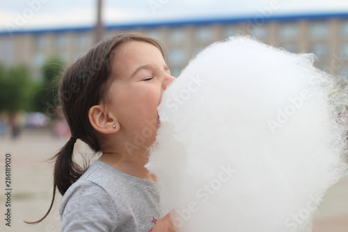 Little girl with pigtails tries to bite a big ball of cotton candy at a city celebration