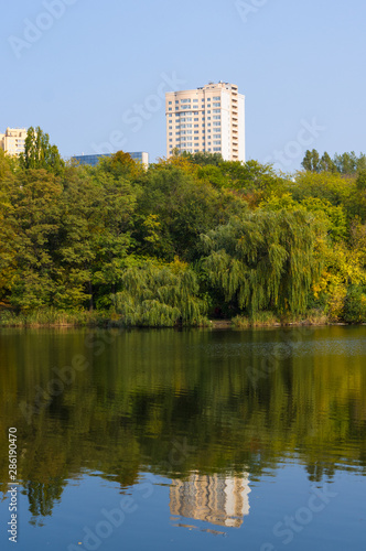 Autumn urban landscape on a Sunny day - yellow autumn trees in the Park, river, and bright sky with clouds © Wingedbull