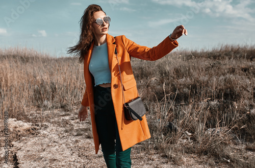 Autumn fashion. Beautiful attracrive young woman in bright autumn look. Orange trendy coat and pants and fashion sunglasses.