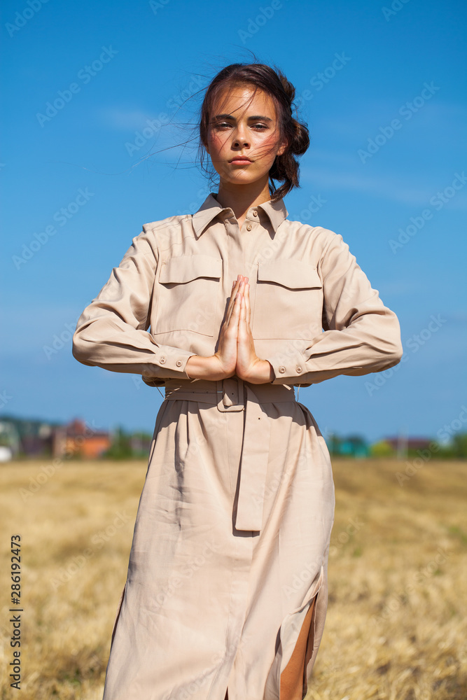 Young beautiful brunette model in a beige dress posing against the background of a mowed wheat field Young beautiful brunette model in a beige dress posing against the background of a mowed wheat field