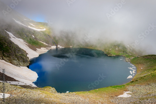 Beautiful misty view of famous the Eye lake on Rila mountain in Bulgaria, sunlit landscape and lots of mountain hikers walking on the highlands