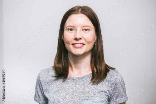 portrait of stylish young pretty Caucasian woman smiling in grey t-shirt on white studio background, isolated, natural look, long brown hair © Elizaveta