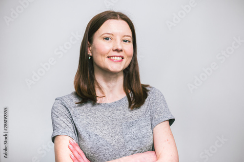 portrait of stylish young pretty Caucasian woman smiling in grey t-shirt on white studio background, isolated, natural look, long brown hair