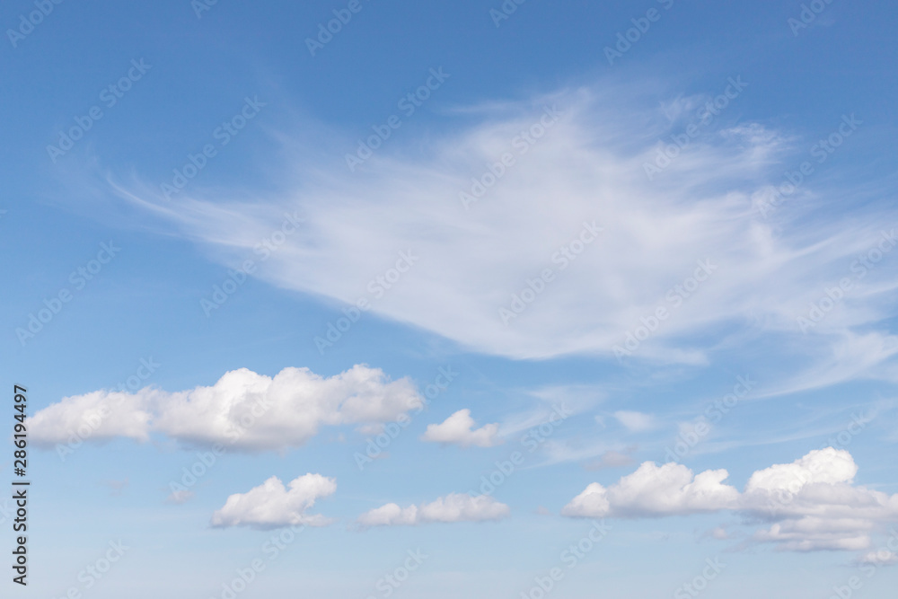 Blue sky with white clouds. In the sky you can see small fluffy white clouds. Feather clouds can also be seen. Sunny weather. Daytime weather. Background with free space and empty place.