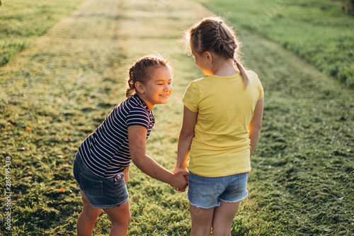Two cheerful caucasian girls holding hands together, hugging, smiling,playing outdoors in summer park. Childhood lifestyle, summer, nature concept