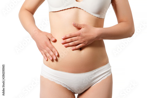 Concept of early term of pregnancy. Close up photo of woman's abdomen and belly button, she is touching her slim stomach with two hands. isolated white background