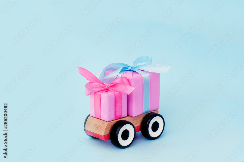 Toy car delivering Christmas gift on blue background. Christmas holiday celebration and new year background concept, copy space. Congratulations on Women's Day, mum's day, Valentine's day, happy birt Toy car delivering Christmas gift on blue background. Christmas holiday celebration and new year background concept, copy space. Congratulations on Women's Day, mum's day, Valentine's day, happy birt