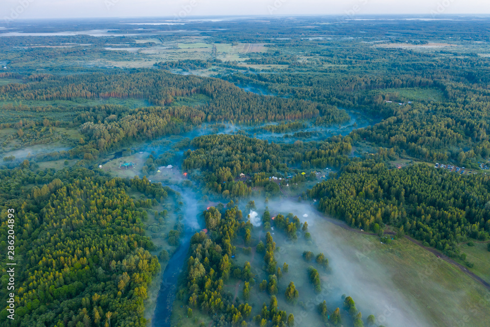 Fototapeta premium Aerial view of the forest, field and river covered with layers of thick morning fog