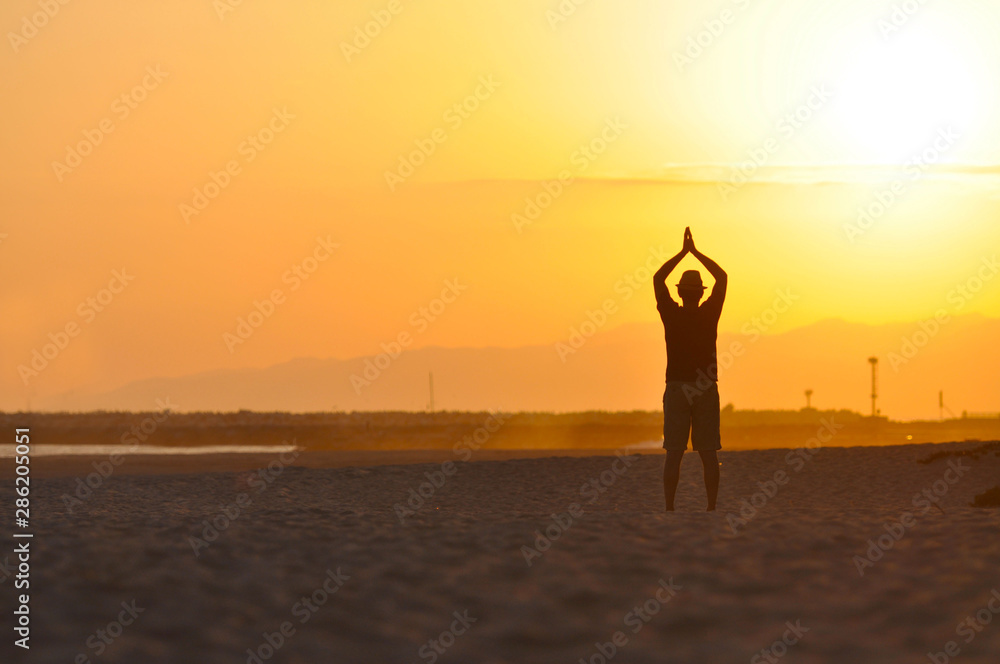 Fototapeta premium Silhouette of a Man on the beach meditating at sunset.