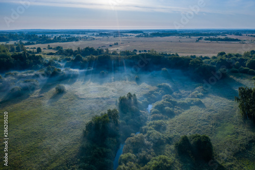 Aerial view of the forest  field and river covered with layers of thick morning fog