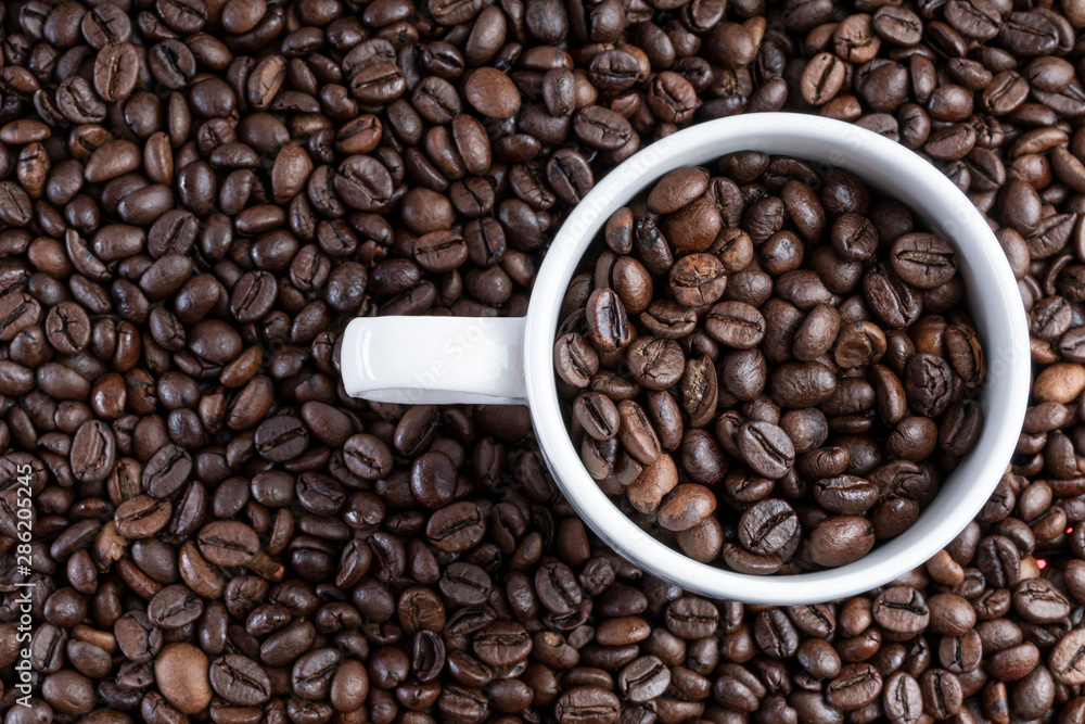 Background of roasted bean coffee with a white cup full of bean coffee on one side. full cup Background of roasted bean coffee with a white cup full of bean coffee on one side. full cup