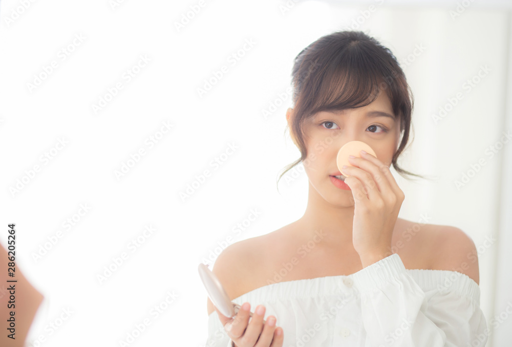 Portrait beautiful young asian woman applying powder puff at cheek makeup of cosmetic looking mirror, beauty of girl with skin face smile in the bedroom, health and wellness concept. Portrait beautiful young asian woman applying powder puff at cheek makeup of cosmetic looking mirror, beauty of girl with skin face smile in the bedroom, health and wellness concept.