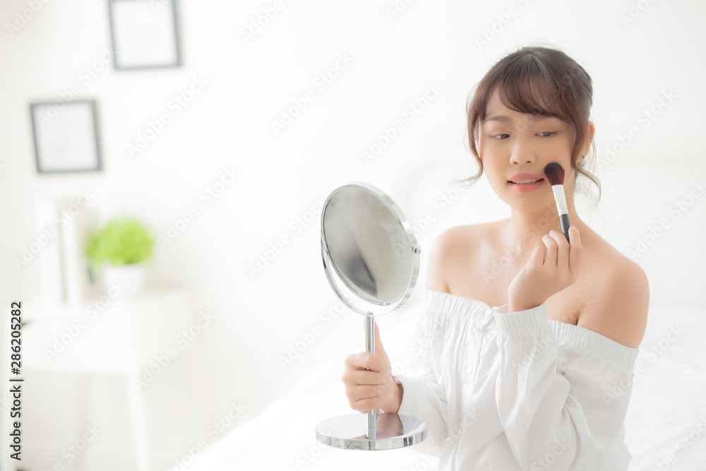 Beauty portrait young asian woman smile with face looking mirror applying makeup with brush cheek in the bedroom, beautiful of girl holding blusher, skin care and cosmetic concept. Beauty portrait young asian woman smile with face looking mirror applying makeup with brush cheek in the bedroom, beautiful of girl holding blusher, skin care and cosmetic concept.