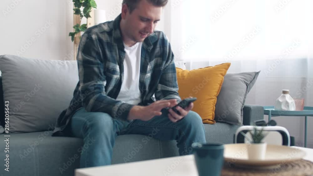 Man seat on the couch in living room and using smartphone. Relaxing after work. Lifestyle. 4k slow motion footage. Man seat on the couch in living room and using smartphone. Relaxing after work. Lifestyle. 4k slow motion footage.
