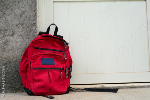 red backpack with zippers and black straps recharged on a white door photo