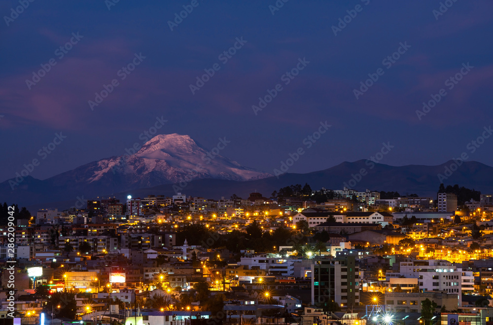 Cityscape of Quito at night with the impressive Cayambe volcano, Andes mountains, Ecuador, South America.