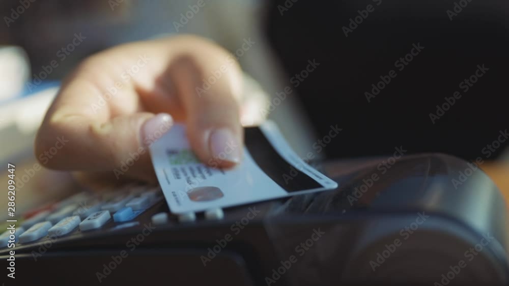 Close-up of woman rotating credit card in hands applying on pos reader for checkout and wireless money transaction. Credit card payment. Outdoor view. Close-up of woman rotating credit card in hands applying on pos reader for checkout and wireless money transaction. Credit card payment. Outdoor view.