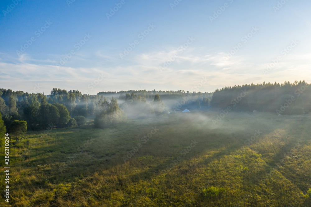 Fog floats over the forest and a field and a star-shaped tent