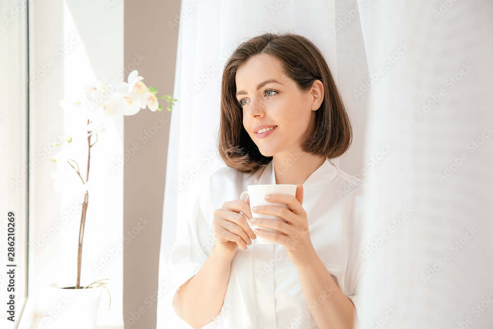 Morning of beautiful young woman drinking coffee near window Morning of beautiful young woman drinking coffee near window