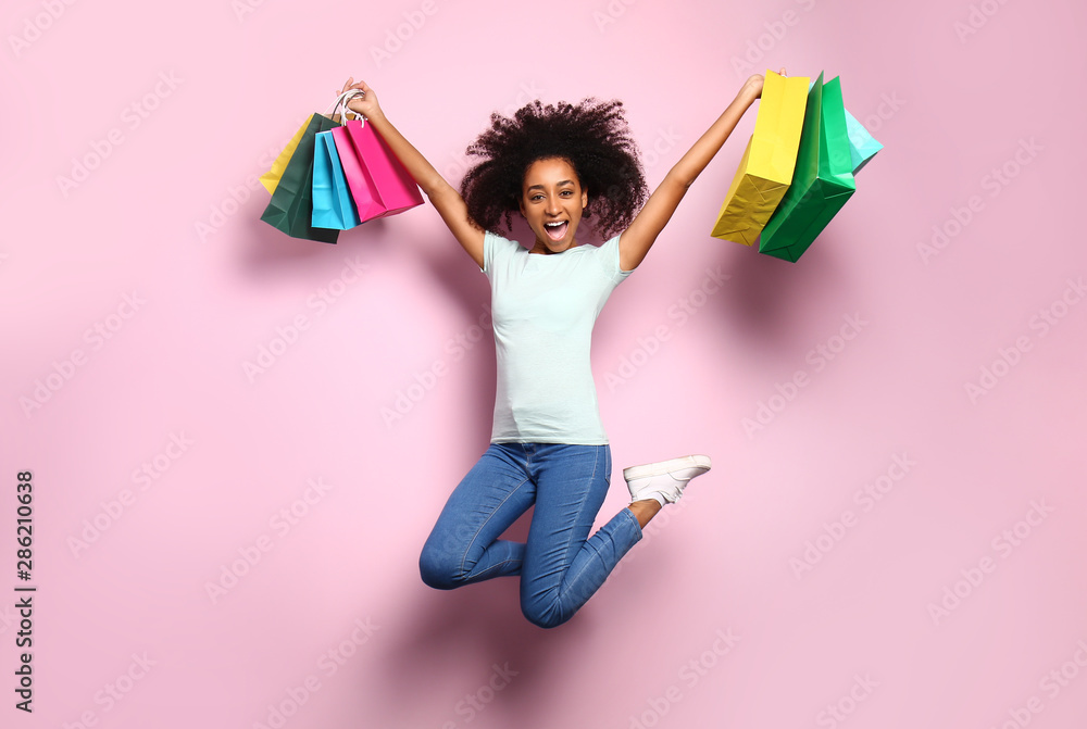Portrait of jumping African-American woman with shopping bags on color background - obrazy, fototapety, plakaty 