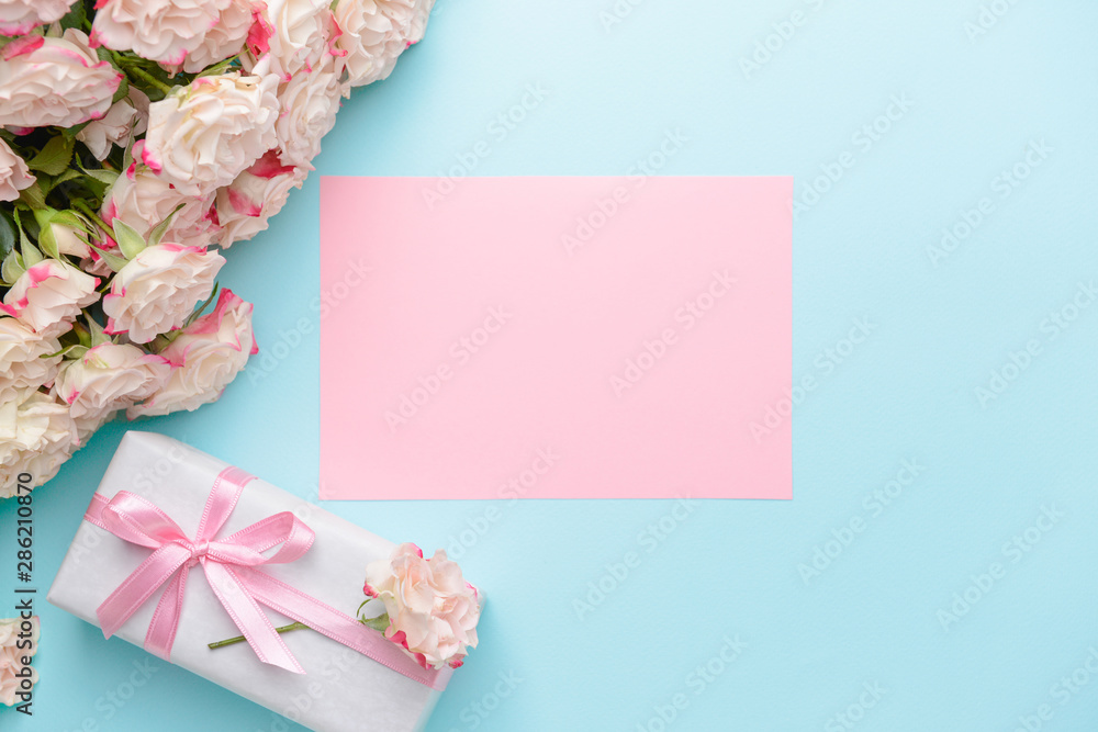 Gift box, blank card and beautiful flowers on color background