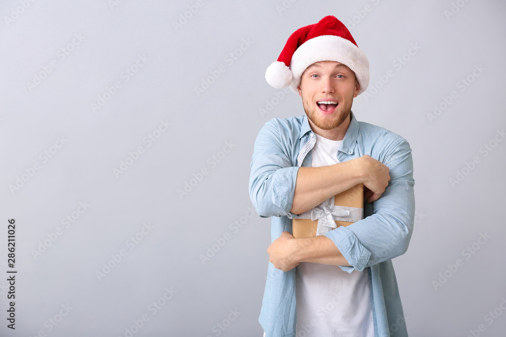 Young man with Christmas gift box on light background