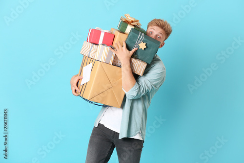 Young man with many gift boxes on color background