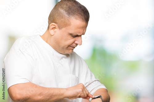 Middle age arab man wearig white t-shirt over isolated background Checking the time on wrist watch, relaxed and confident photo