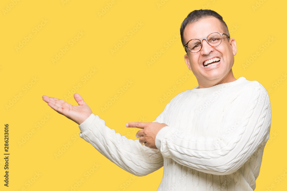 Middle age arab man wearing glasses over isolated background amazed and smiling to the camera while presenting with hand and pointing with finger. Middle age arab man wearing glasses over isolated background amazed and smiling to the camera while presenting with hand and pointing with finger.