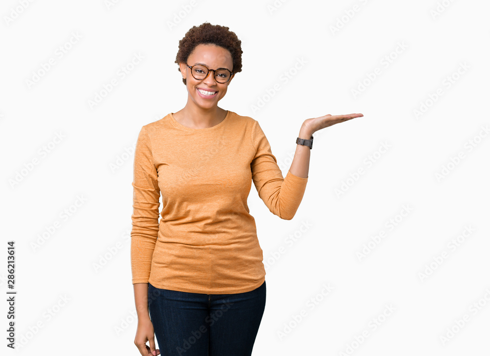 Young beautiful african american woman wearing glasses over isolated background smiling cheerful presenting and pointing with palm of hand looking at the camera. Young beautiful african american woman wearing glasses over isolated background smiling cheerful presenting and pointing with palm of hand looking at the camera.