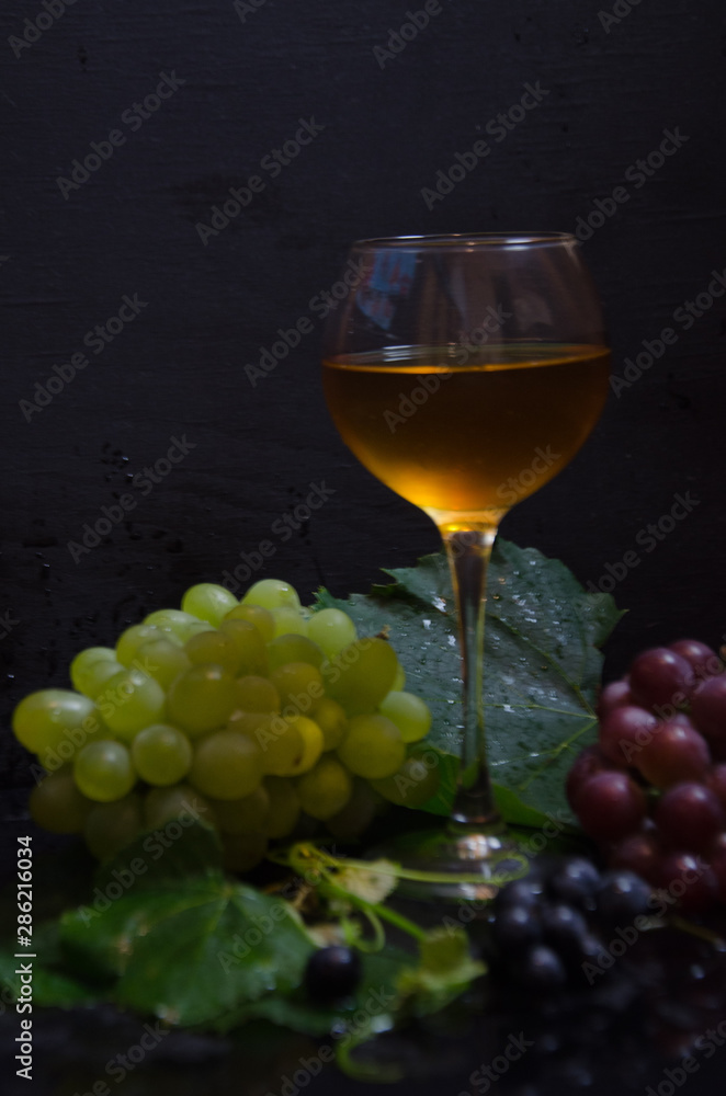 grape brush and leaves and wine glass on black background selective focus